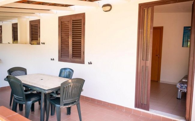 Veranda con tavolo, sedie in plastica nera e persiane marroni.