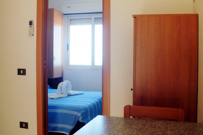 Camera con finestra, armadio e letto col copriletto blu.