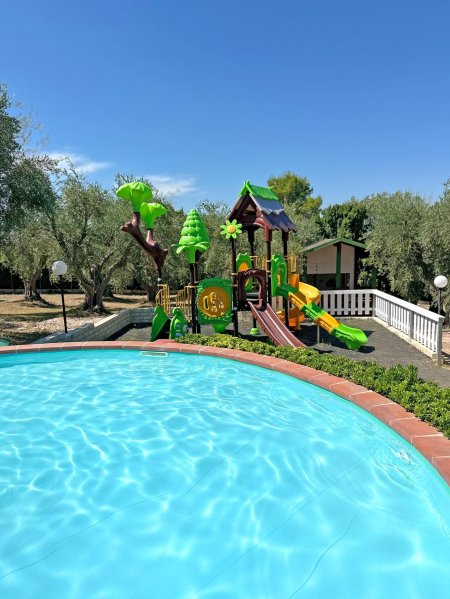 Piscina rotonda con parco giochi colorato sullo sfondo.